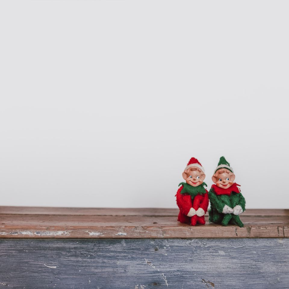 Two elves sitting on a shelf against a white background