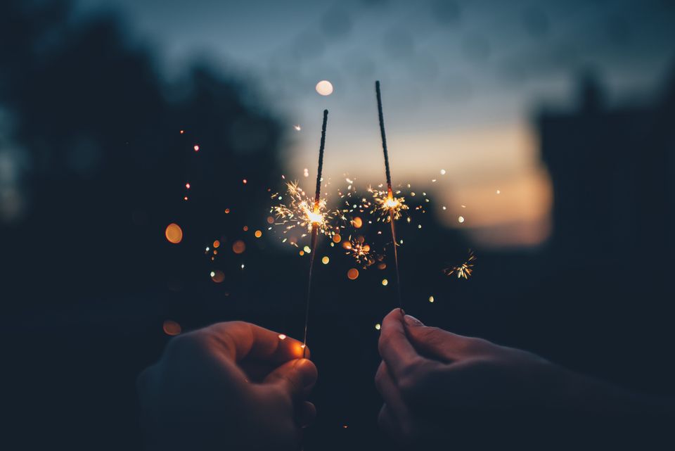 Two hands hold a sparkler each against a blurred sunset