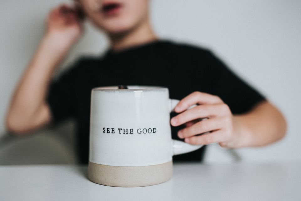 A white ceramic mug with a cream ring at the bottom with the words "See the Good"