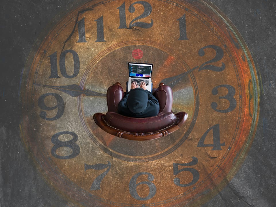 Person sits on leather armchair with a laptop balanced on their lap. On the floor is a large clock painted on the floor. 